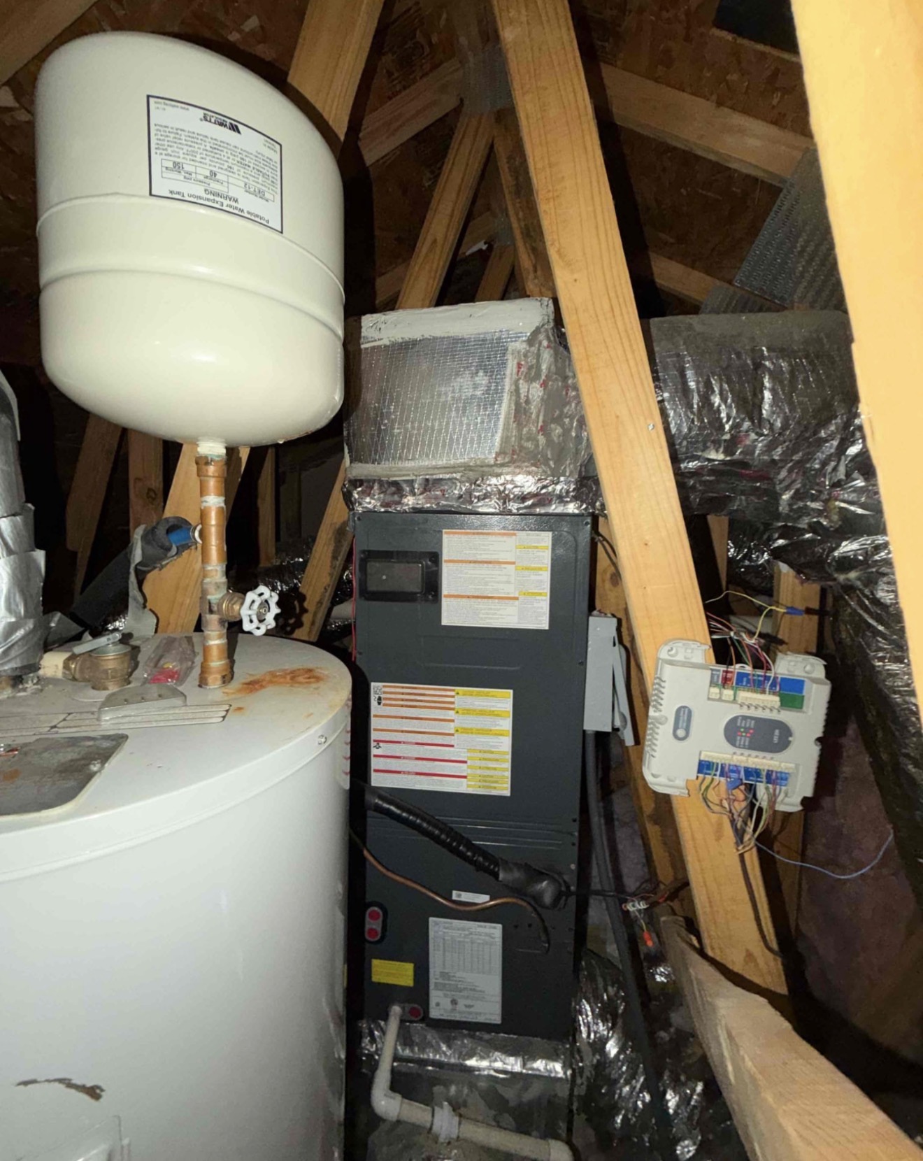 Attic air handler installation showing foil-wrapped media air cleaner, zone control board mounted on framing for multi-zone temperature management, and clean condensate routing
